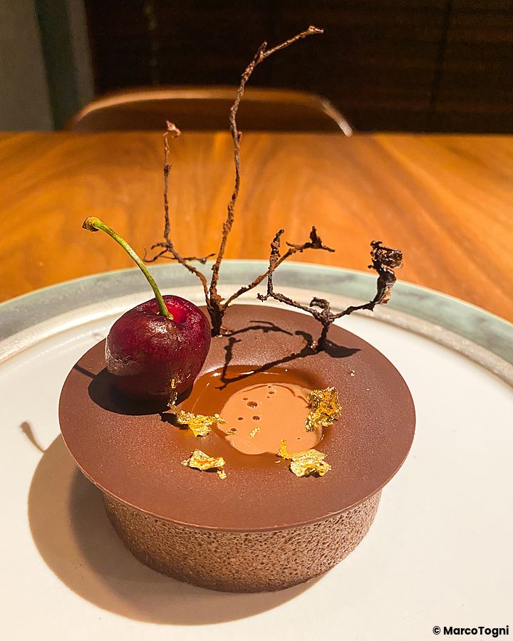 Dolce al cioccolato con ciliegia e scaglie d'oro su un piatto bianco servito al ristorante Le Sputnik a Tokyo.
