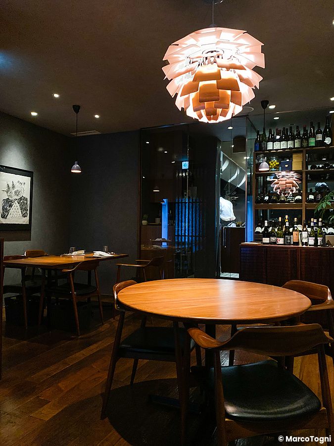 Interno del ristorante Le Sputnik a Tokyo con tavoli in legno, sedie e una grande lampada a sospensione.