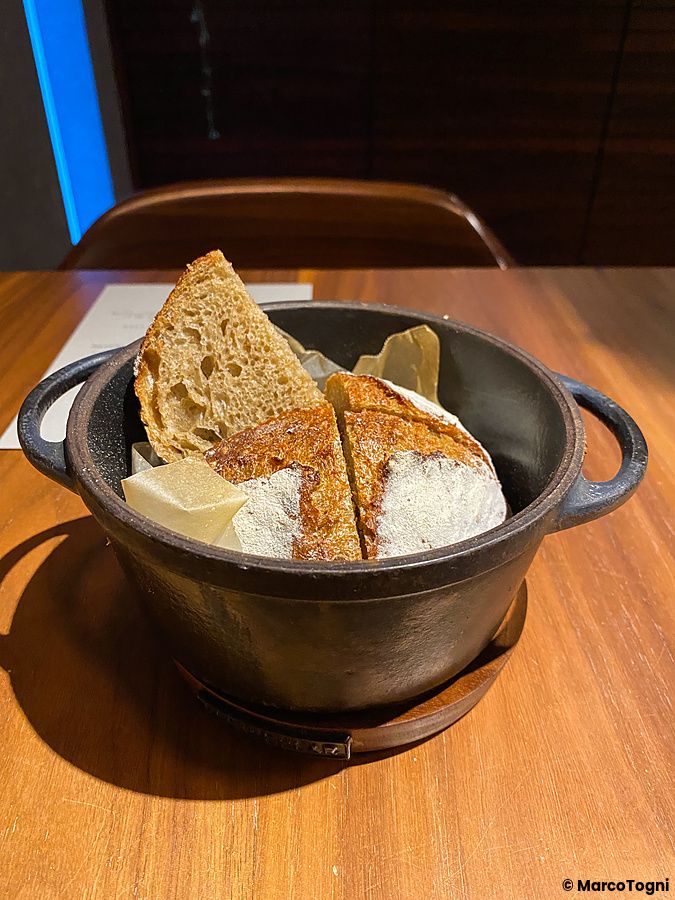 Pane artigianale a fette servito in un recipiente di ghisa scuro presso il ristorante Le Sputnik a Tokyo.