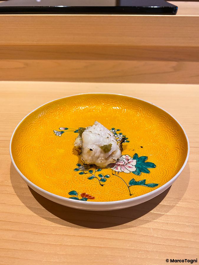 Un boccone di anago grigliato e salsa allo yuzu servito su un piattino giallo decorato da Sushi Masashi a Tokyo.