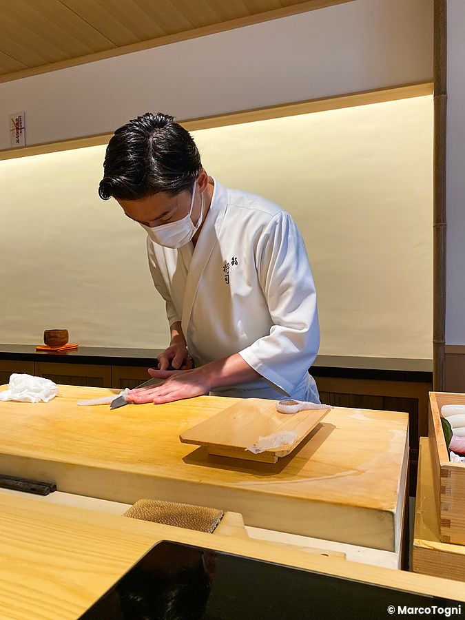 Lo chef Masashi Yamaguchi al lavoro con un coltello sul bancone in legno da Sushi Masashi a Tokyo.