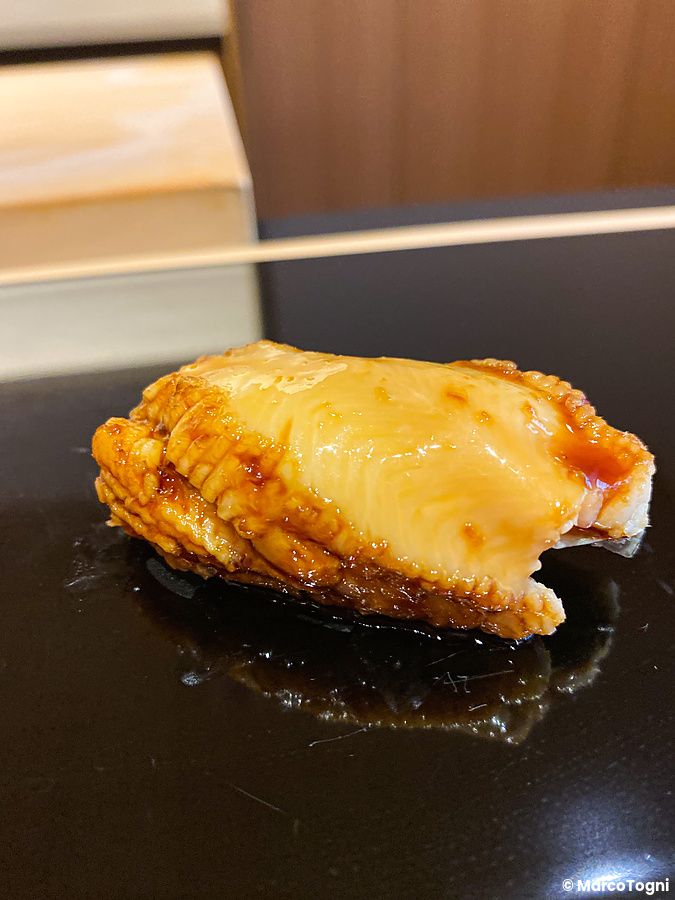 Un nigiri di anago lucido con salsa tare posizionato su una base scura da Sushi Masashi.