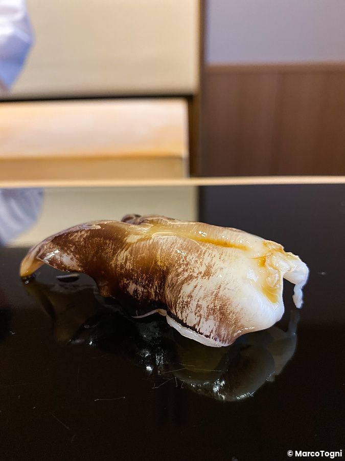 Un nigiri di hokkigai è servito su una superficie scura riflettente da Sushi Masashi a Tokyo.