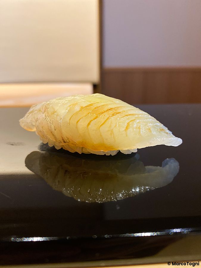 Un nigiri di sayori poggiato su un piano nero lucido da Sushi Masashi a Tokyo.