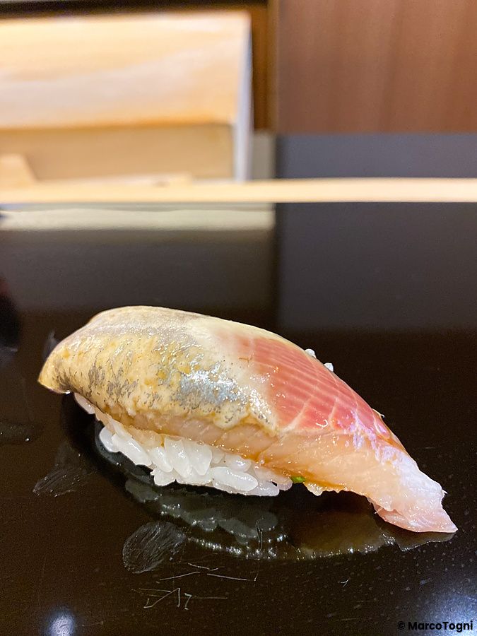 Un nigiri di shima aji è posizionato su un vassoio nero lucido all'interno del ristorante Sushi Masashi a Tokyo.