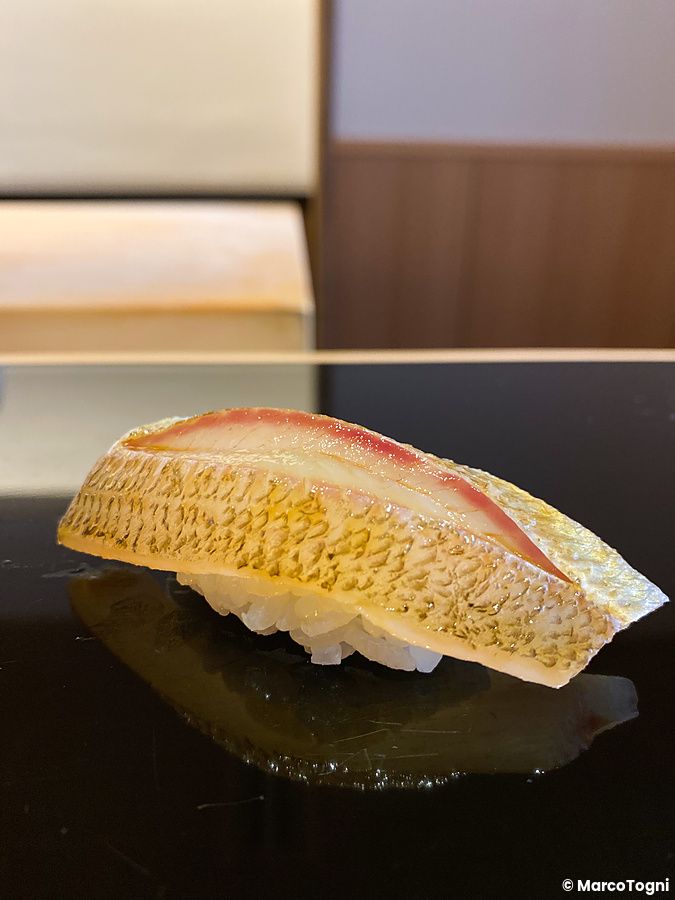 Un nigiri di sayori servito su un vassoio nero lucido da Sushi Masashi a Tokyo.