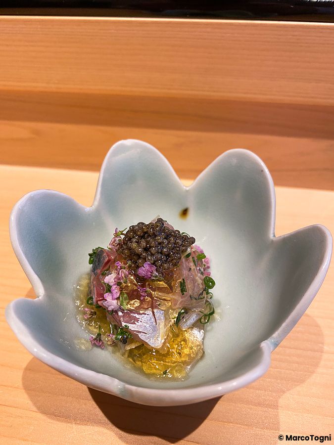 Una composizione di pesce azzurro, fiori di shiso e caviale servita in una ciotola a forma di fiore da Sushi Masashi.