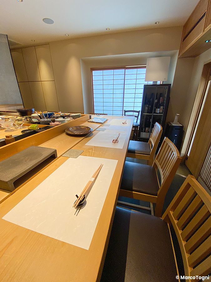 Veduta interna del bancone a Sushi Takeuchi con sedute in legno e apparecchiatura minimalista.