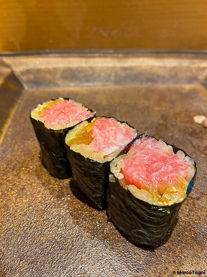 Tre pezzi di maki con tonno disposti in fila su un piatto di ceramica scura da Sushi Takeuchi a Tokyo.