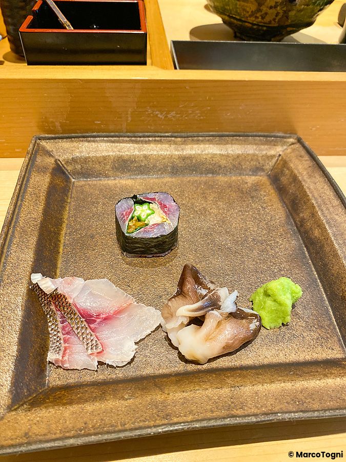 Piatto con mollusco torigai, pesce isawki e un maki servito su un bancone di legno da Sushi Takeuchi a Tokyo.
