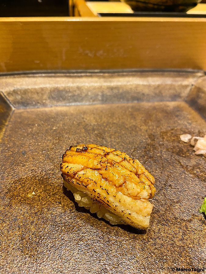 Nigiri di anago posizionato su un piatto in ceramica scura da Sushi Takeuchi.