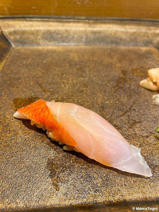 Un nigiri di kinmedai servito su un piatto scuro da Sushi Takeuchi.