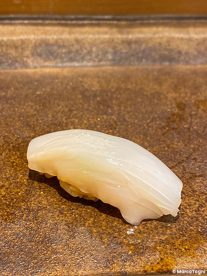 Un nigiri di sumi ika servito su un piatto scuro da Sushi Takeuchi.