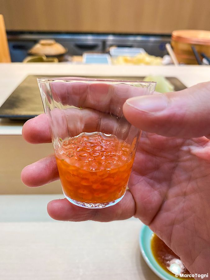 Una mano di una persona tiene un bicchiere con ikura presso il ristorante Sushi Tou a Tokyo.