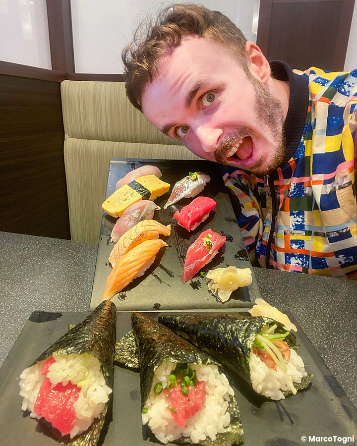 Marco Togni entusiasta con piatto di sushi assortito in un ristorante giapponese.