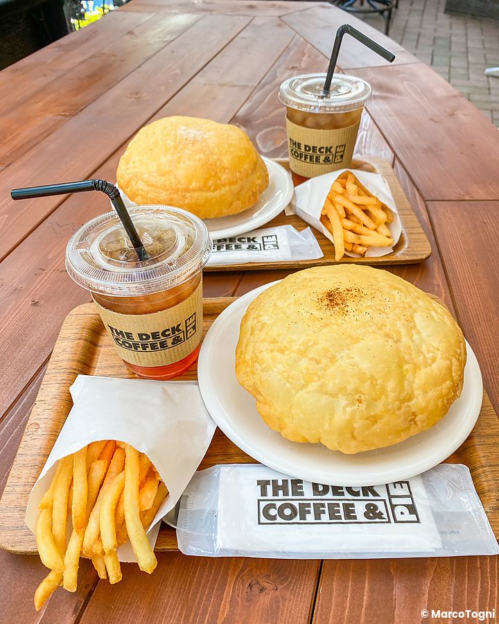 Due vassoi con hot pie, porzioni di patatine fritte e bicchieri di caffè presso The Deck Coffee & Pie a Tokyo.