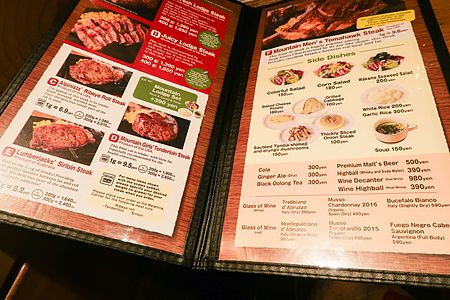 Un menu cartaceo del ristorante Steak Lodge in Giappone che elenca vari tagli di carne e contorni con i relativi prezzi.