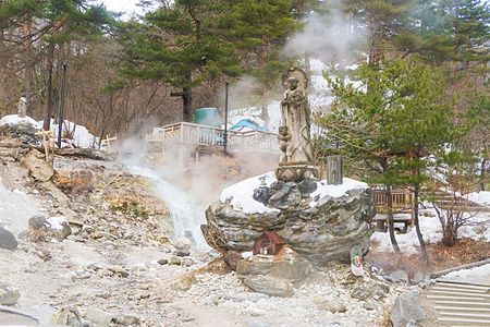 Statua di pietra circondata da vapore termale su una roccia nevosa presso il Sainokawara Park a Kusatsu Onsen.