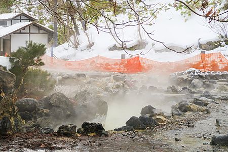 Veduta invernale di Sainokawara Park a Kusatsu Onsen con vapore che sale dalle sorgenti tra rocce e neve.