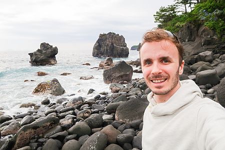 Marco Togni sorride in un selfie scattato davanti alle scogliere e alle rocce vulcaniche della Costa di Jogasaki.