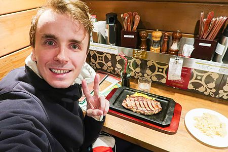 Marco Togni sorridente fa il gesto della vittoria davanti a una bistecca di manzo a Steak Lodge in un locale in Giappone.
