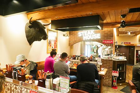 Clienti seduti al bancone del ristorante Steak Lodge in Giappone con una testa di toro decorativa sulla parete.