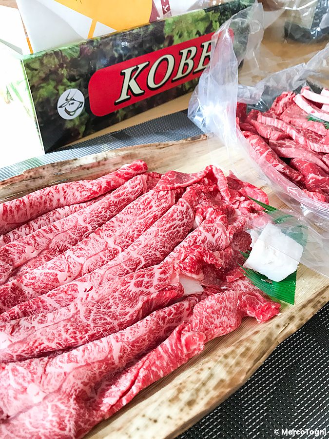 Carne di Kobe cruda, ricevuta tramite corriere a casa, disposta su un vassoio in legno accanto alla scatola originale.