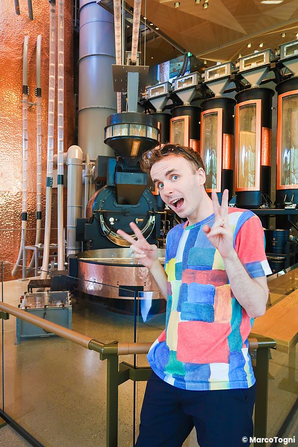 Marco Togni sorride facendo il segno di vittoria davanti ai macchinari della torrefazione a Starbucks Reserve.