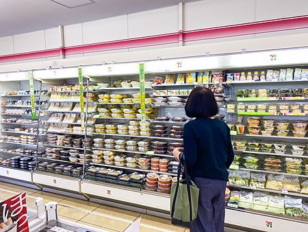 Persona davanti a un frigorifero in un conbini in Giappone con vari cibi pronti sugli scaffali.
