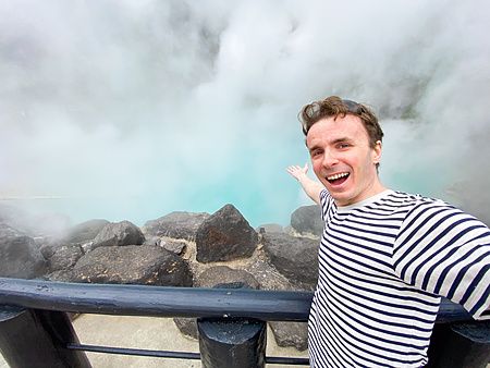 Marco Togni posa per un selfie davanti alla sorgente termale Umi Jigoku a Beppu con vapore bianco che sale dall'acqua blu.