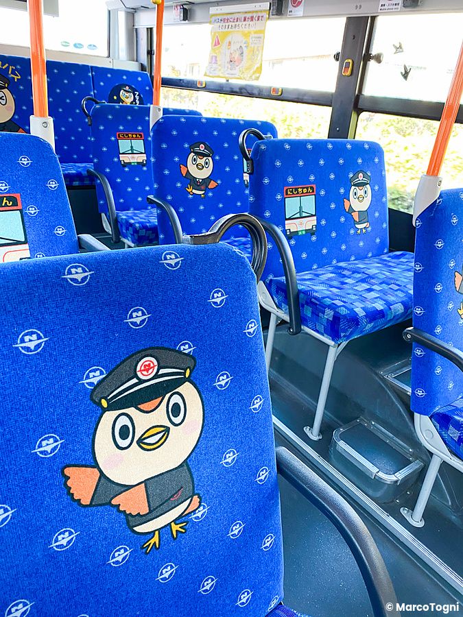 Interno di un autobus kawaii in Giappone con sedili blu decorati da disegni di una mascotte con cappello da capotreno.