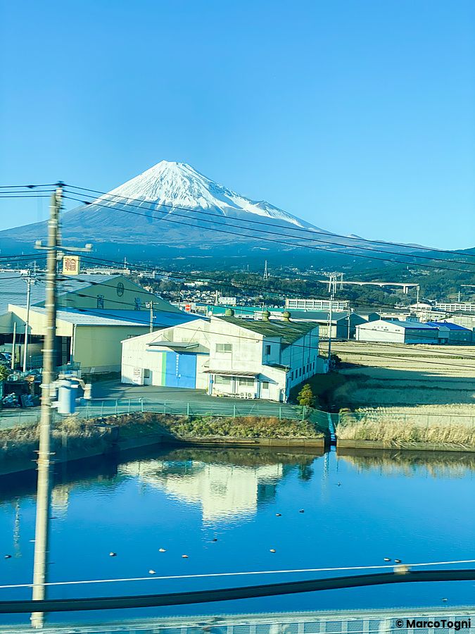 Vista del Monte Fuji dal treno shinkansen con edifici in primo piano.