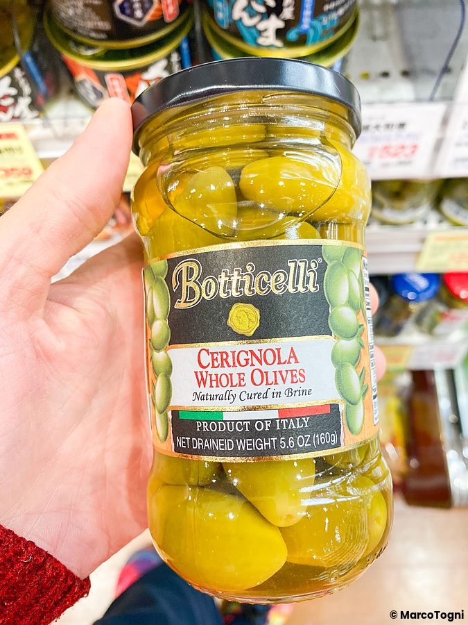 Un barattolo di olive Cerignola Botticelli tenuto in mano da una persona all'interno del negozio Seijo Ishii.