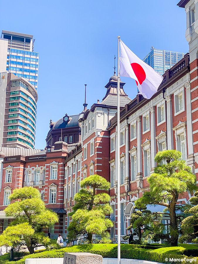 Bandiera del Giappone che sventola davanti alla storica facciata in mattoni rossi della stazione di Tokyo.