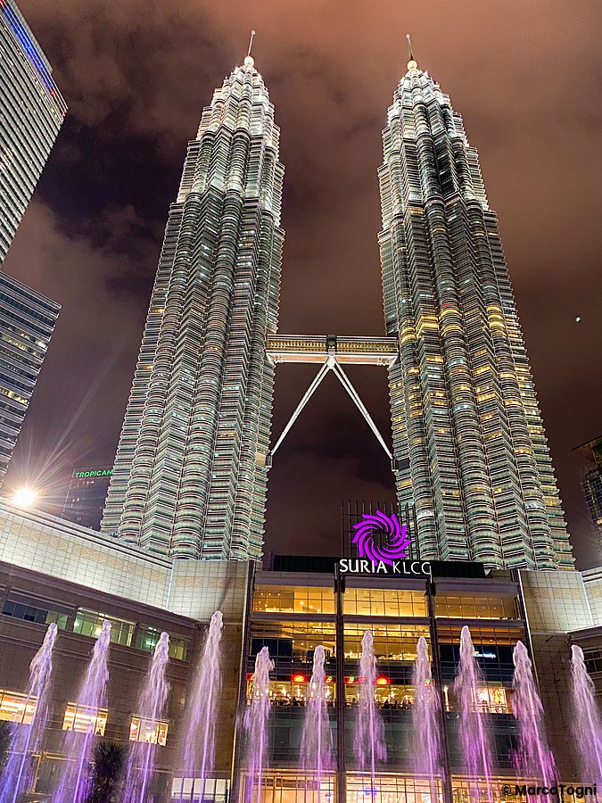 Le Torri Petronas illuminate di notte a Kuala Lumpur con fontane in primo piano.
