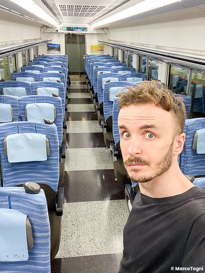 Marco Togni in un treno giapponese con sedili blu, vagone quasi vuoto.