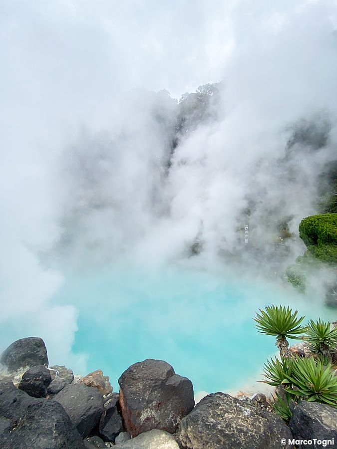 Le acque turchesi e il vapore denso di Umi Jigoku a Beppu tra rocce vulcaniche e vegetazione.