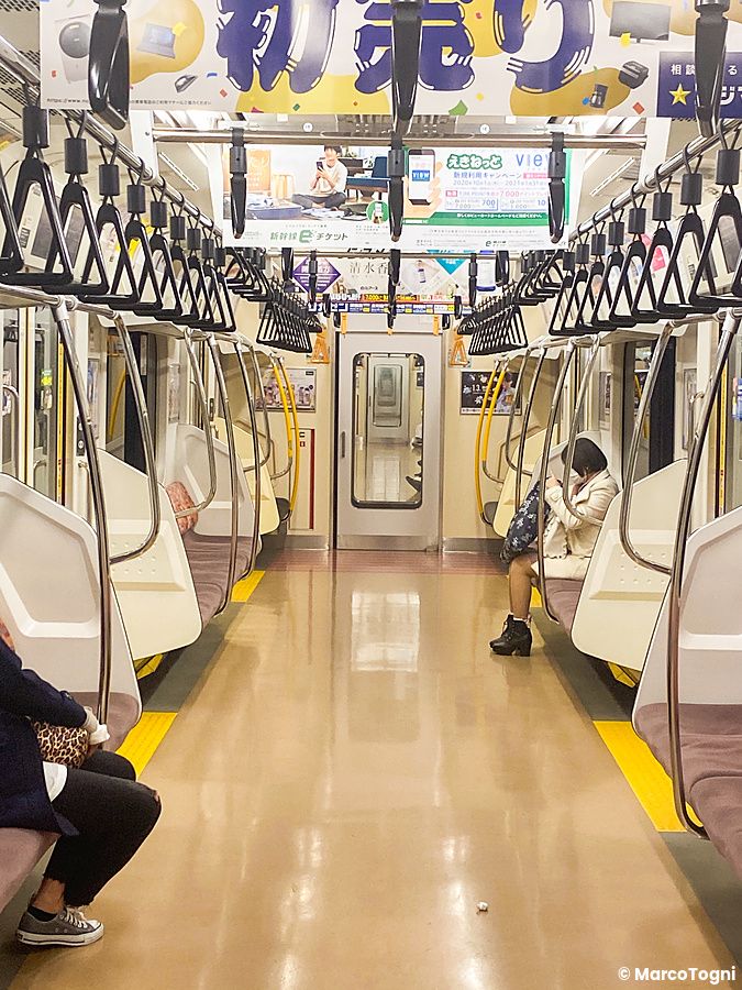 Interno di un vagone treno giappone in Giappone con una persona seduta sulla destra e maniglie appese al soffitto.