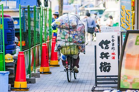 Uomo su bicicletta con carico di bottiglie di plastica in una via giapponese.