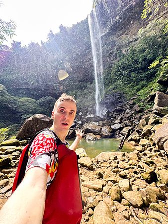 Marco Togni davanti alla cascata di Pinaisara a Okinawa, circondato dalla natura.