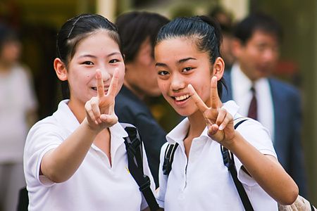 Due giovani a Shibuya che fanno il segno della pace sorridendo.