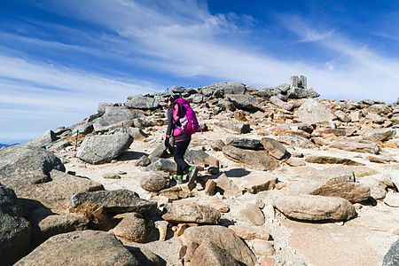 Una persona con uno zaino rosa cammina su un sentiero di rocce verso la vetta del Monte Kisokoma.