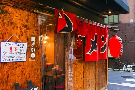 Ingresso in legno di un ristorante ramen in Giappone con tende noren rosse e una lanterna rossa appesa.