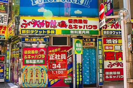 Facciata colorata del centro informazioni di servizi per adulti a Shibuya con cartelloni.