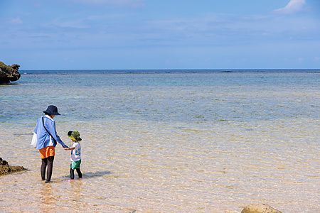 Una persona adulta e un bambino camminano mano nella mano nelle acque basse e trasparenti della spiaggia Hoshizuma.