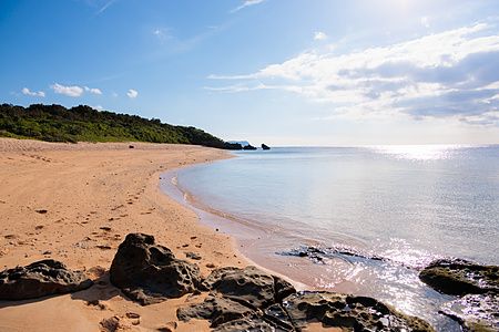 Veduta della spiaggia Mimikiri sull'isola di Iriomote a Okinawa con sabbia dorata, rocce scure e mare calmo.