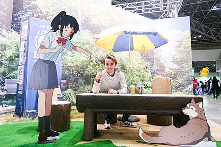 Marco Togni seduto a un tavolo tra le sagome in cartone di personaggi anime presso la Tokyo Anime Fair a Tokyo.