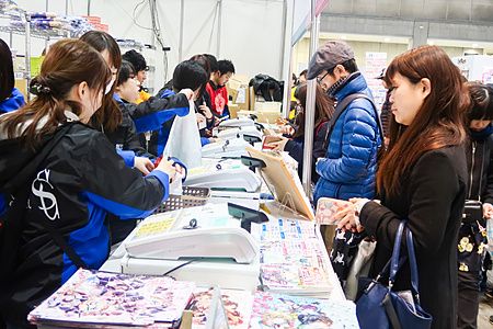Persone in fila presso gli stand di vendita durante la Tokyo Anime Fair con merce esposta sui banchi.