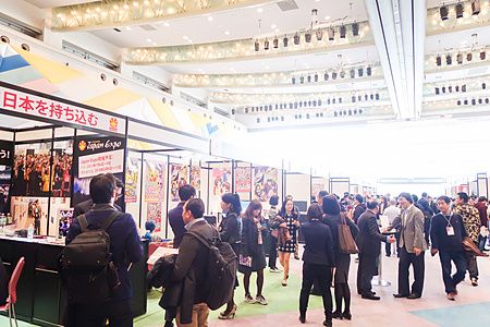 Veduta interna di uno spazio fieristico affollato durante la Tokyo Anime Fair con persone che osservano vari stand.