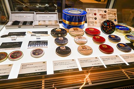 Vetrina espositiva di Caviar House & Prunier a Tokyo con latte di caviale colorate e accessori su piano luminoso.